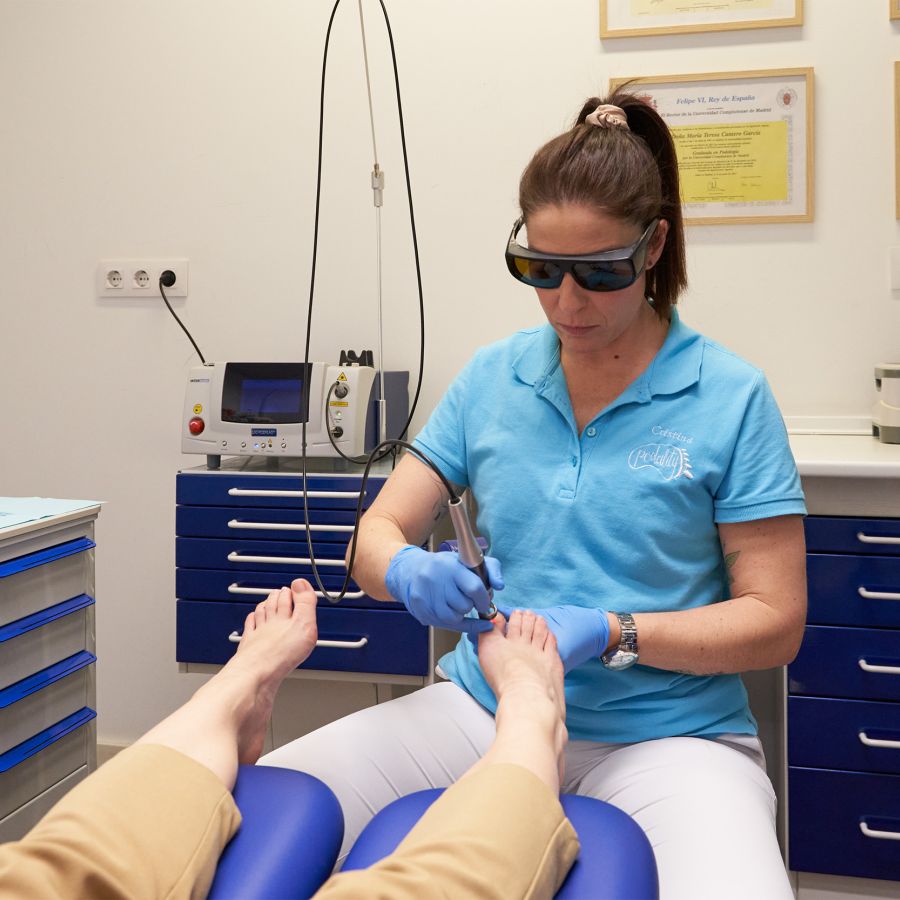 Imagen de profesional con gafas puestas anti rayos tratando el pie con laser de una clienta 
